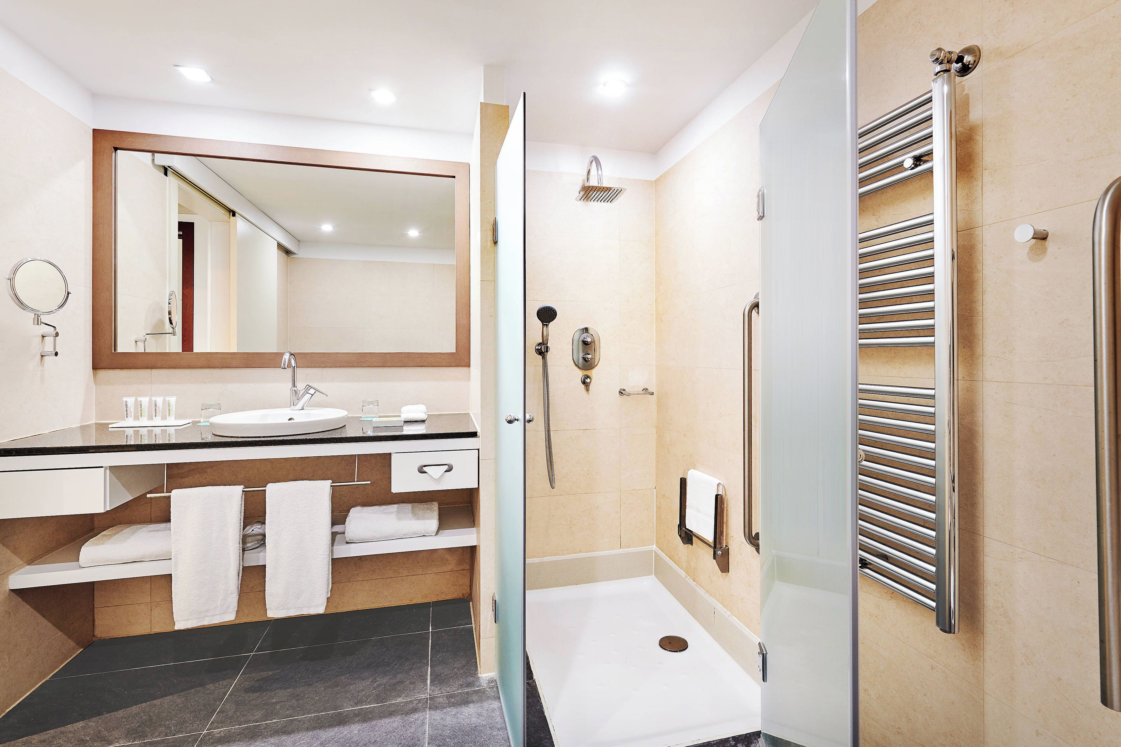 A modern bathroom with a sink, mirror, towel rack, and a glass-enclosed shower area.