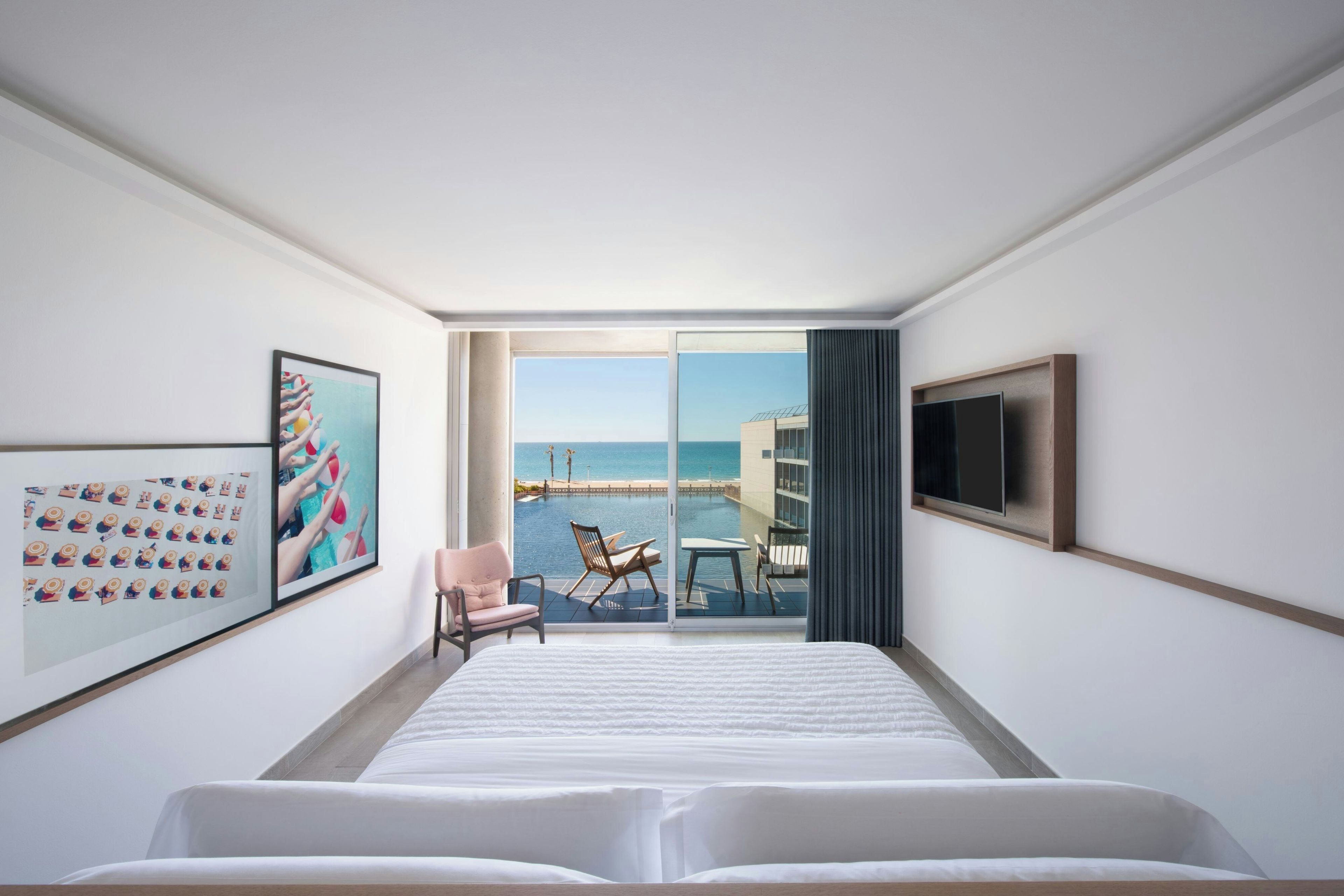 Una habitación de hotel con una cama grande, un televisor, un cuadro enmarcado y vistas al mar a través de una puerta corrediza.