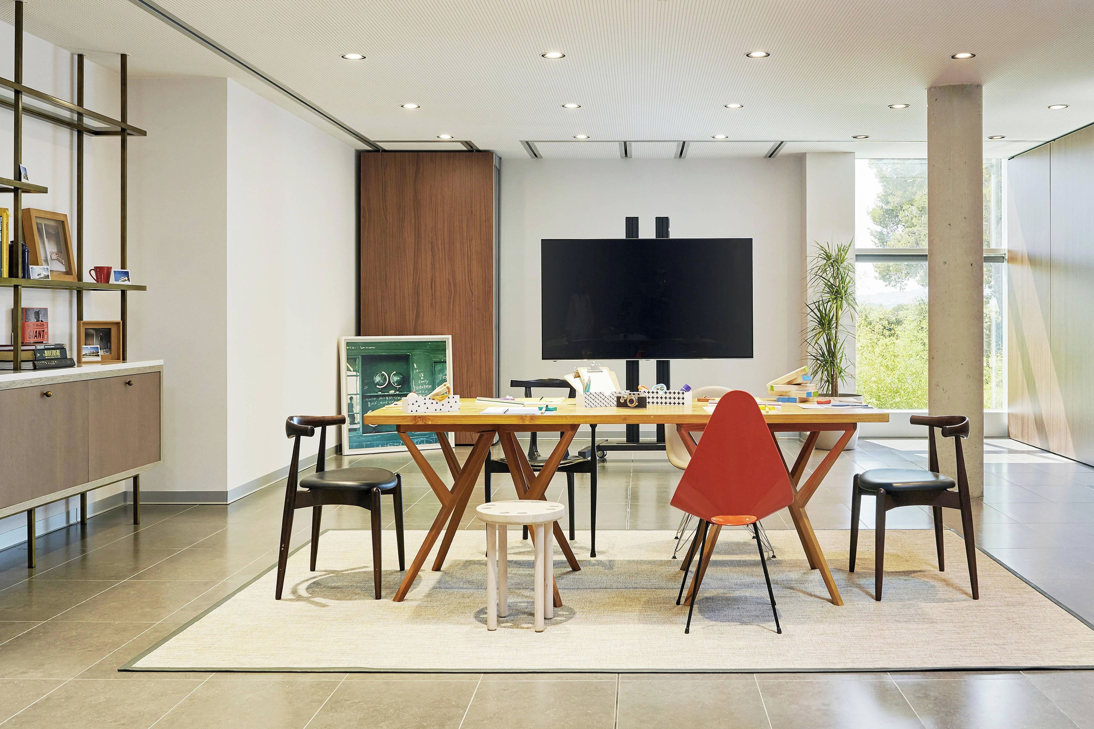 Uma sala de jantar moderna com uma mesa grande, cadeiras e uma tela de televisão.