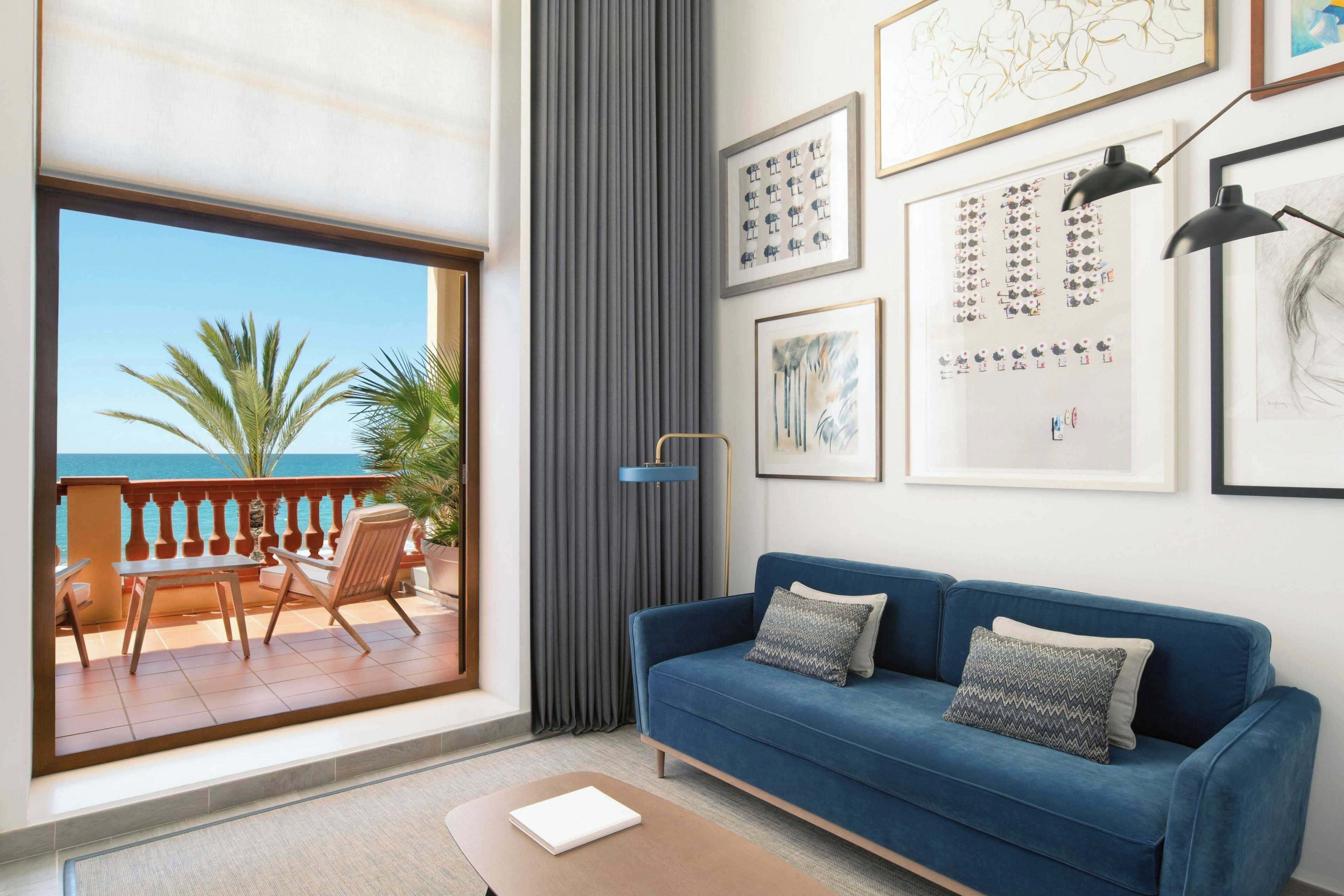 Una sala de estar con un sofá azul, una mesa de madera y vista al mar desde un balcón.