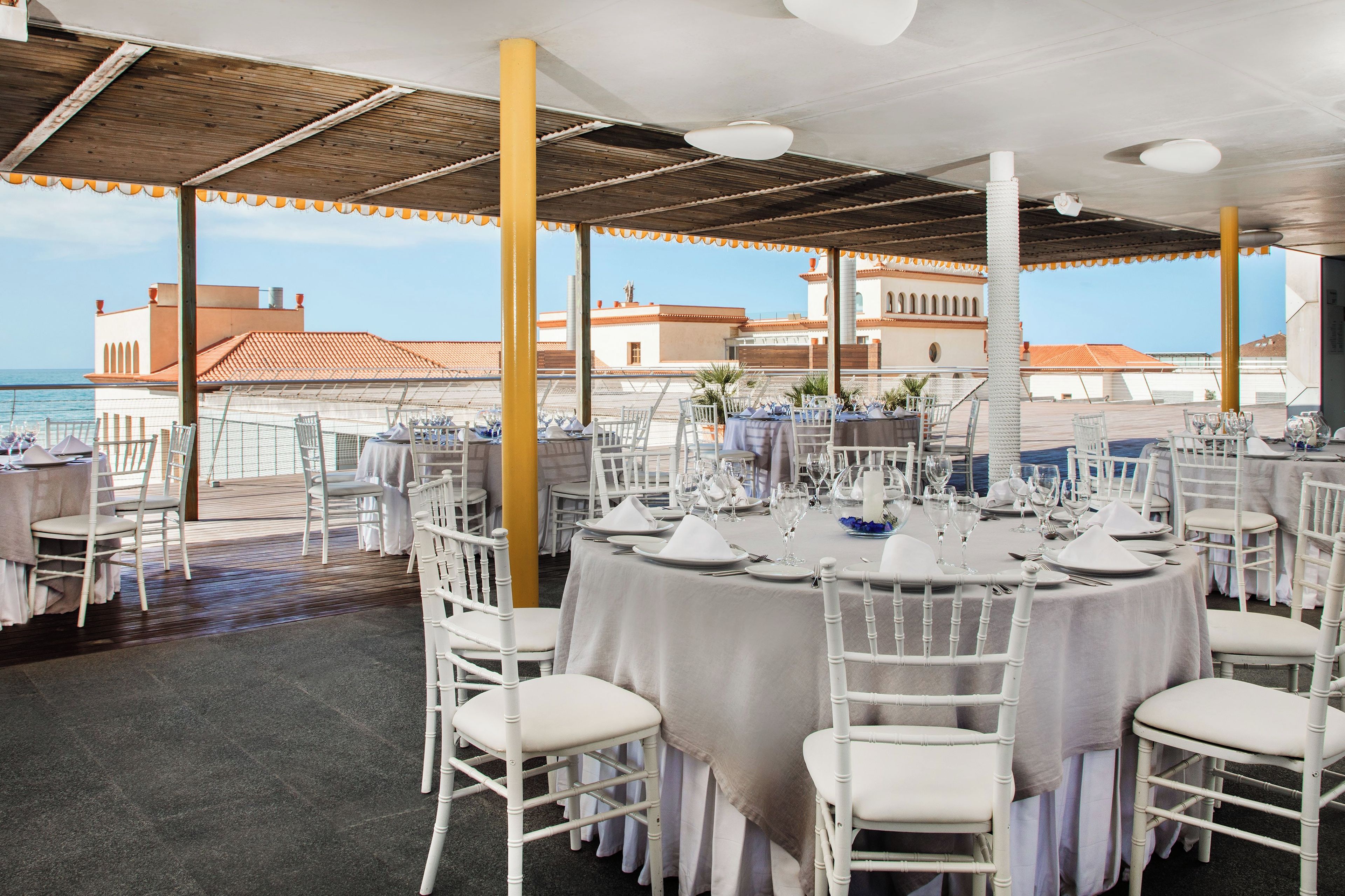 Un área de comedor en la azotea con mesas y sillas blancas, con vista al mar.