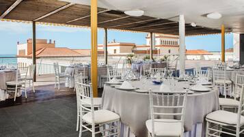 Un área de comedor en la azotea con mesas y sillas blancas, con vista al mar.