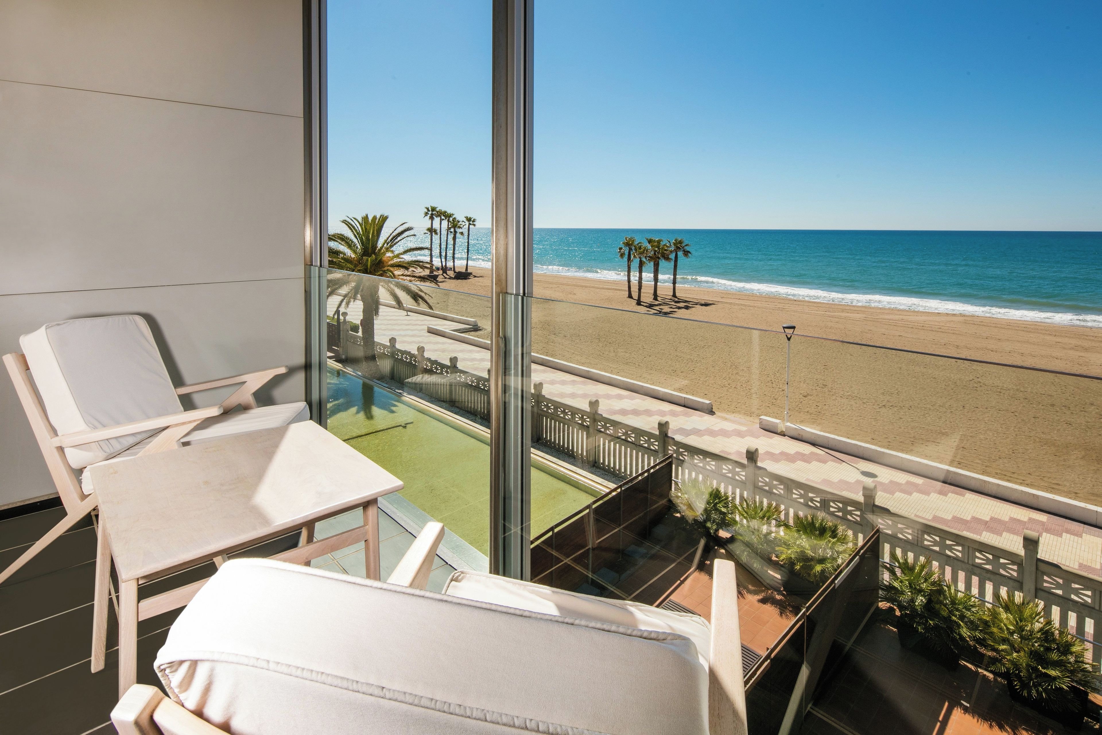Een balkon met uitzicht op een strand, een zwembad en ligstoelen.