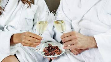 Dos personas vestidas de blanco sostienen copas de vino y una bandeja con trozos de chocolate.