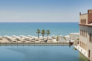 A poolside view with a clear view of the sea, palm trees, and beach umbrellas. - Le Meridien Ra Beach Hotel & Spa (El Vendrell)
