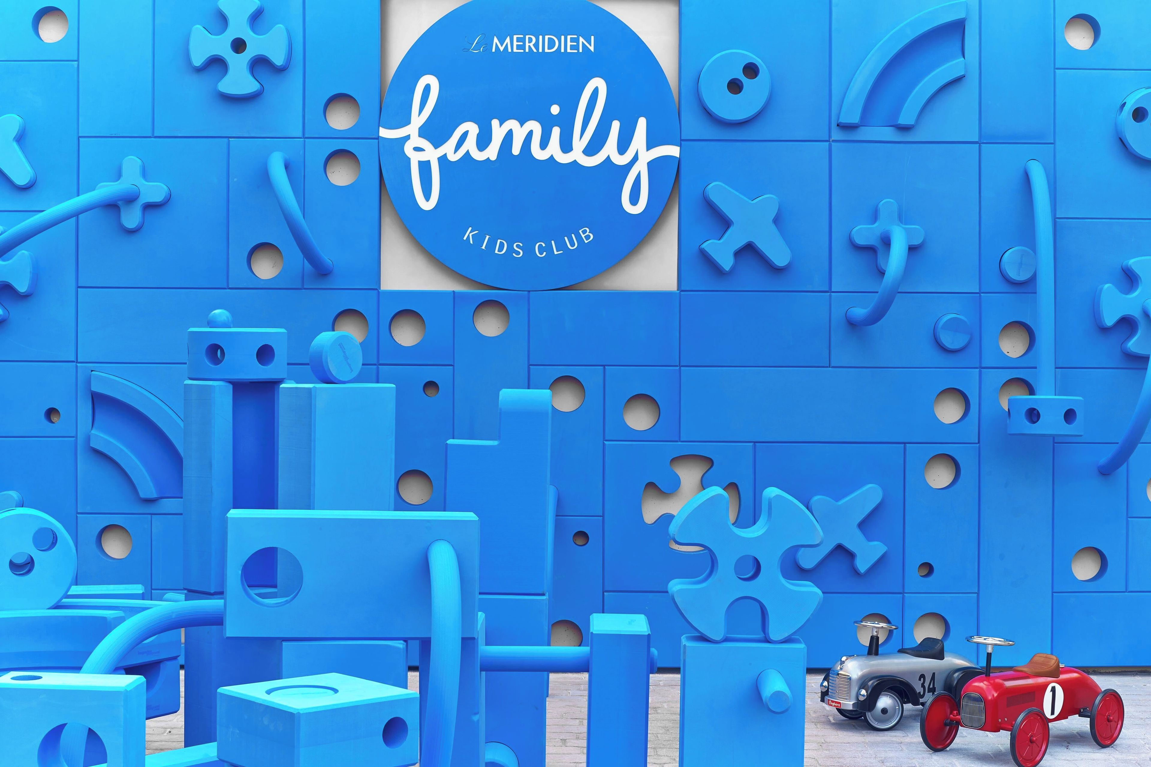 Zona de juegos temática en azul, con estructuras similares a rompecabezas y dos coches de juguete.