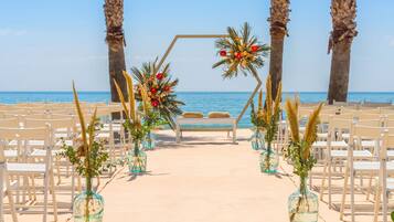 A beach wedding setup with a clear view of the sea, arranged chairs, and palm trees.