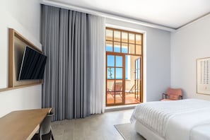 A hotel room with a bed, a desk, a chair, a TV, and a view of the outside. - Le Meridien Ra Beach Hotel & Spa (El Vendrell)
