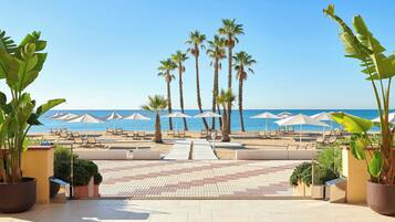 Un resort frente a la playa con palmeras, sillas de playa, sombrillas y una vista despejada del océano.