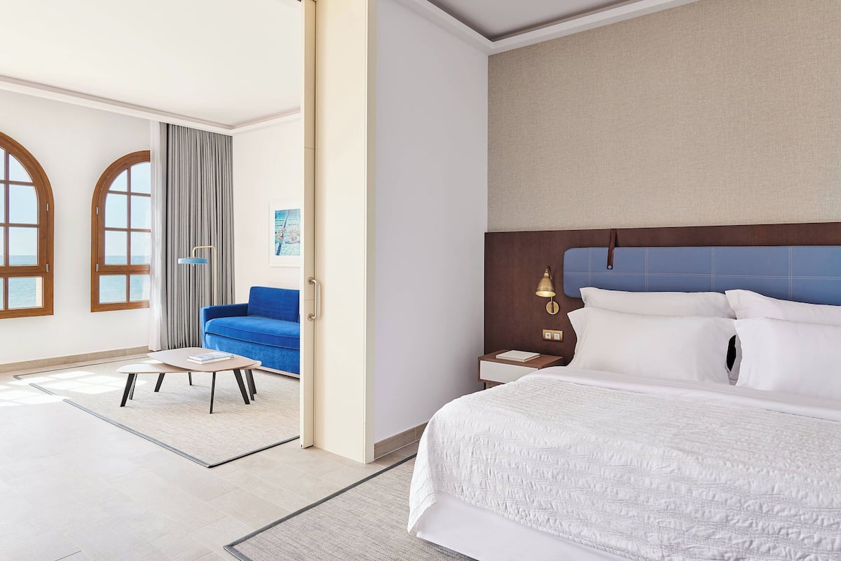 A hotel room with a large bed, a blue sofa, a small table, and a window with curtains.
