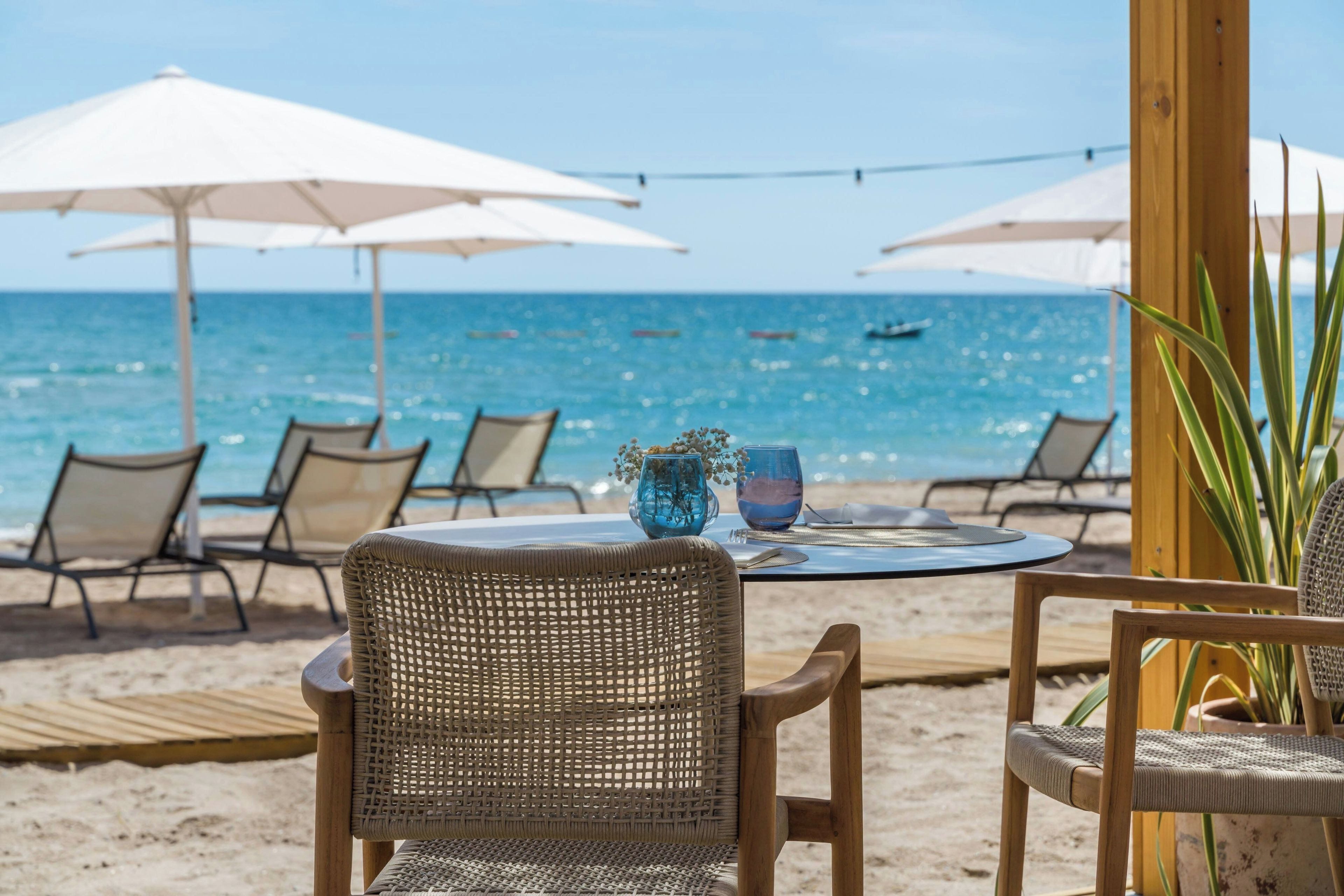 Une table avec des chaises et des parasols, installée sur la plage, avec vue sur la mer.