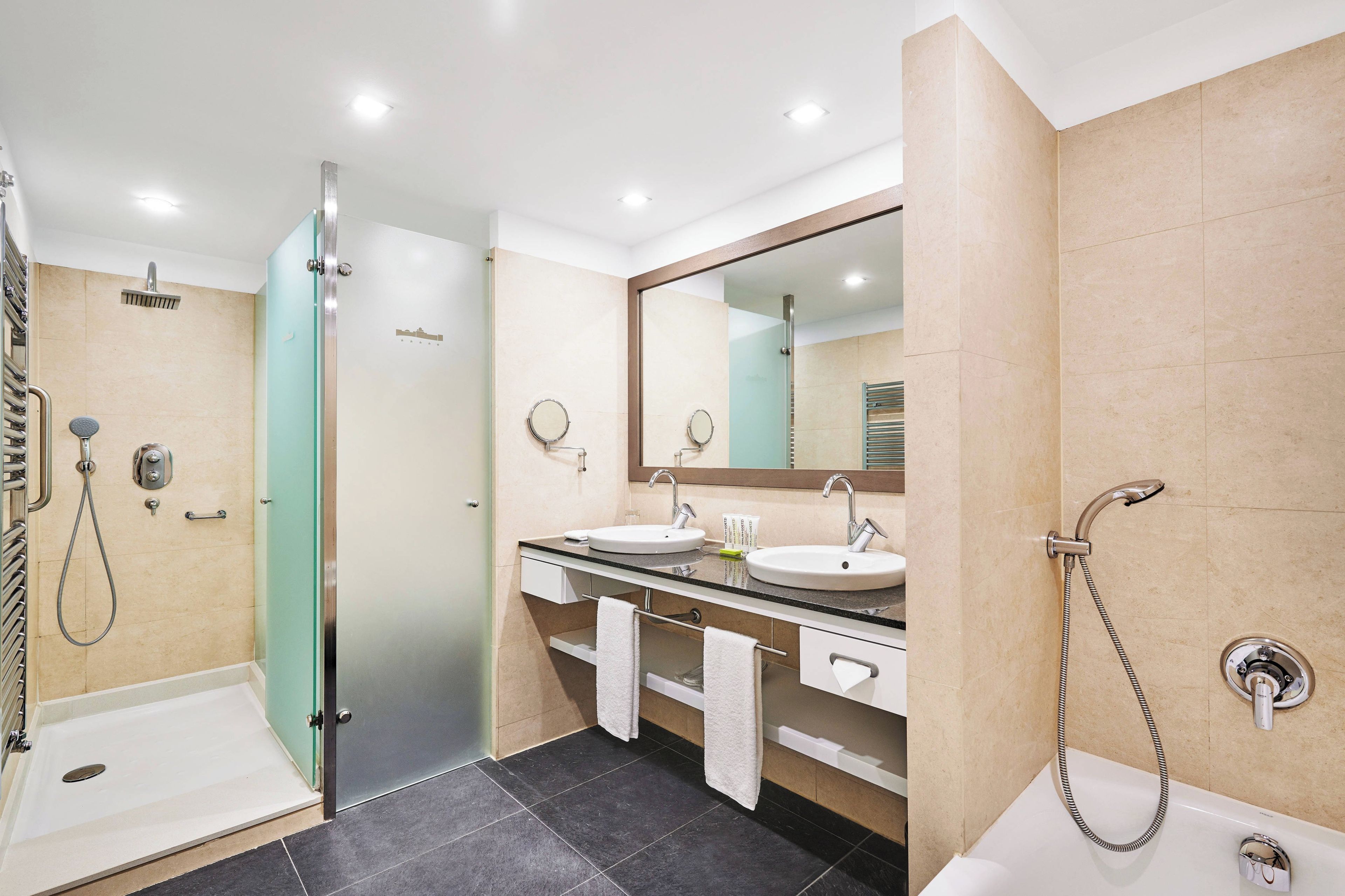 A modern bathroom with two sinks, a glass shower enclosure, and a bathtub.