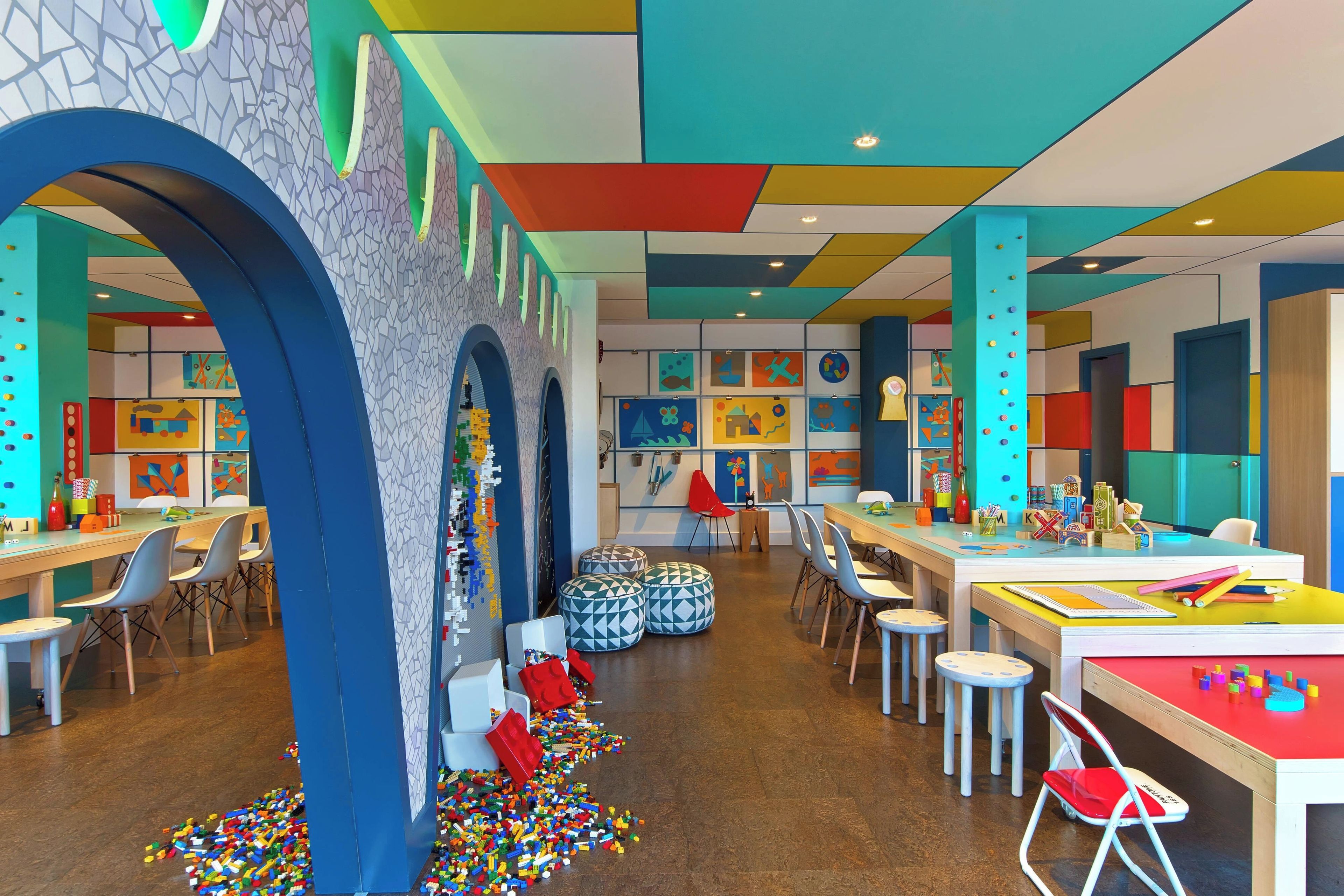 Un área de juegos infantil, luminosa y llena de color, con mesas, sillas y decoraciones alegres.