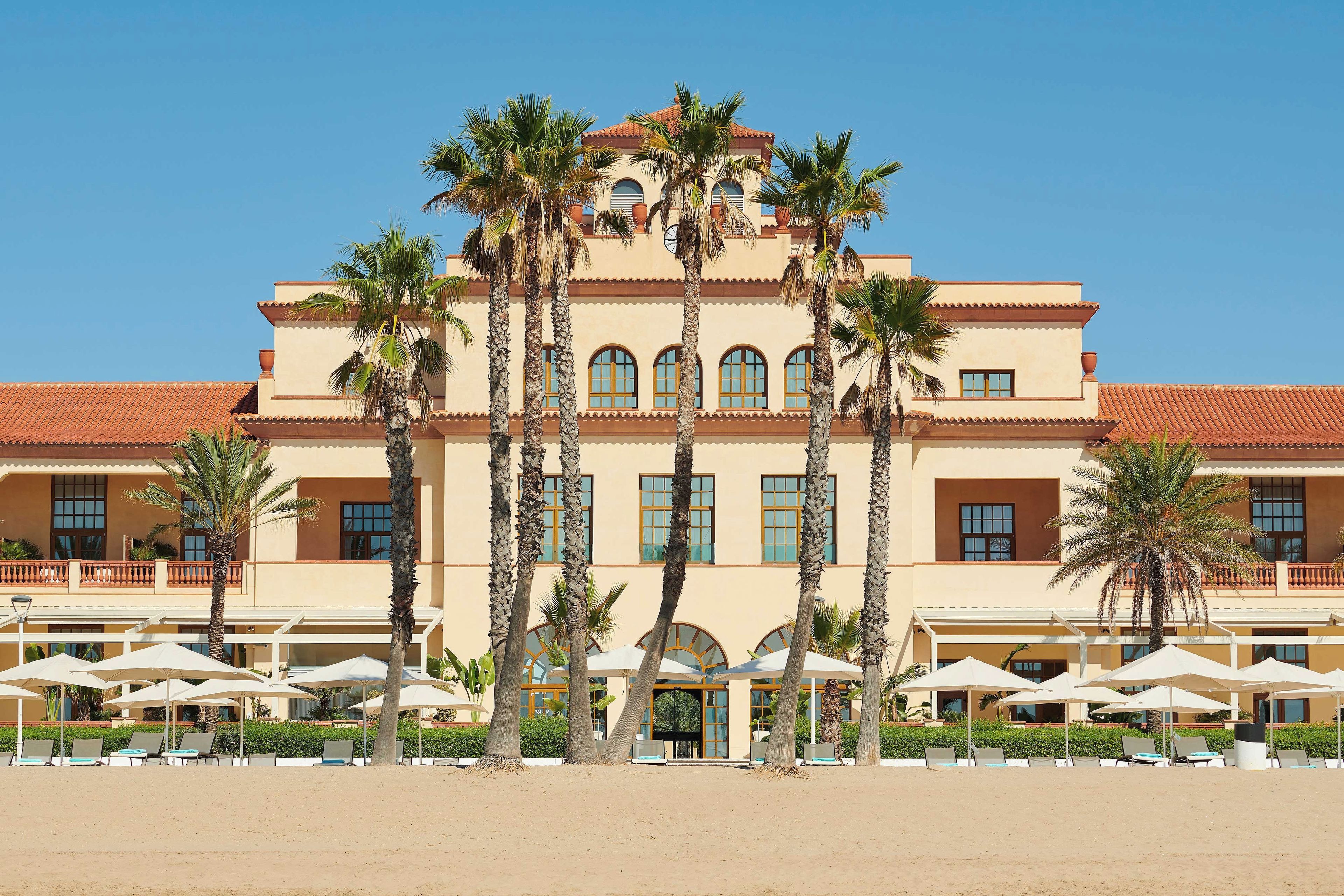 Un hotel grande con varios pisos, palmeras y zonas de estar al aire libre.