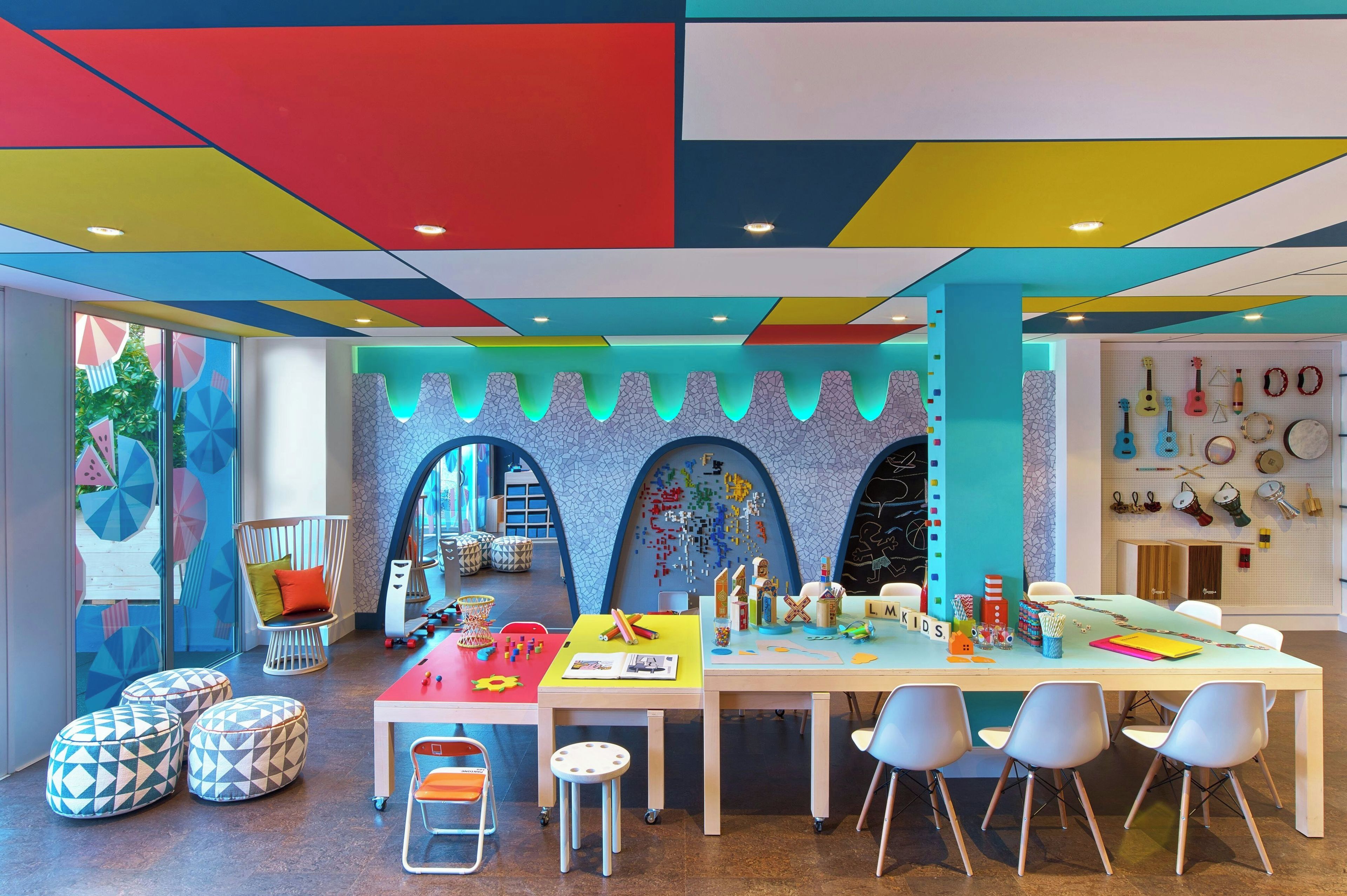 Een levendige kinderspeelruimte met kleurrijke geometrische ontwerpen aan het plafond, een speeltafel en diverse speelgoed.