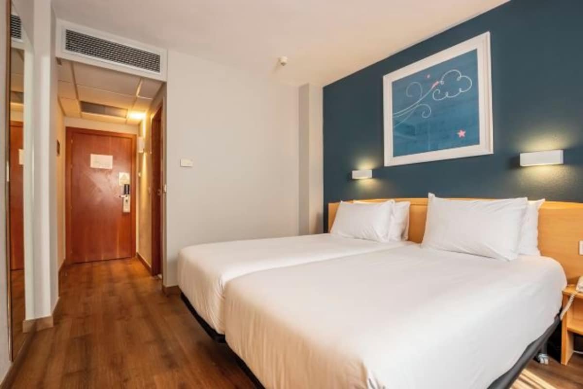 Habitación de hotel con una cama grande, suelo de madera, una pared de acento azul oscuro y una obra de arte enmarcada.