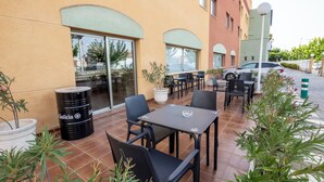 Un patio al aire libre con mesas, sillas, un barril negro y plantas en macetas.