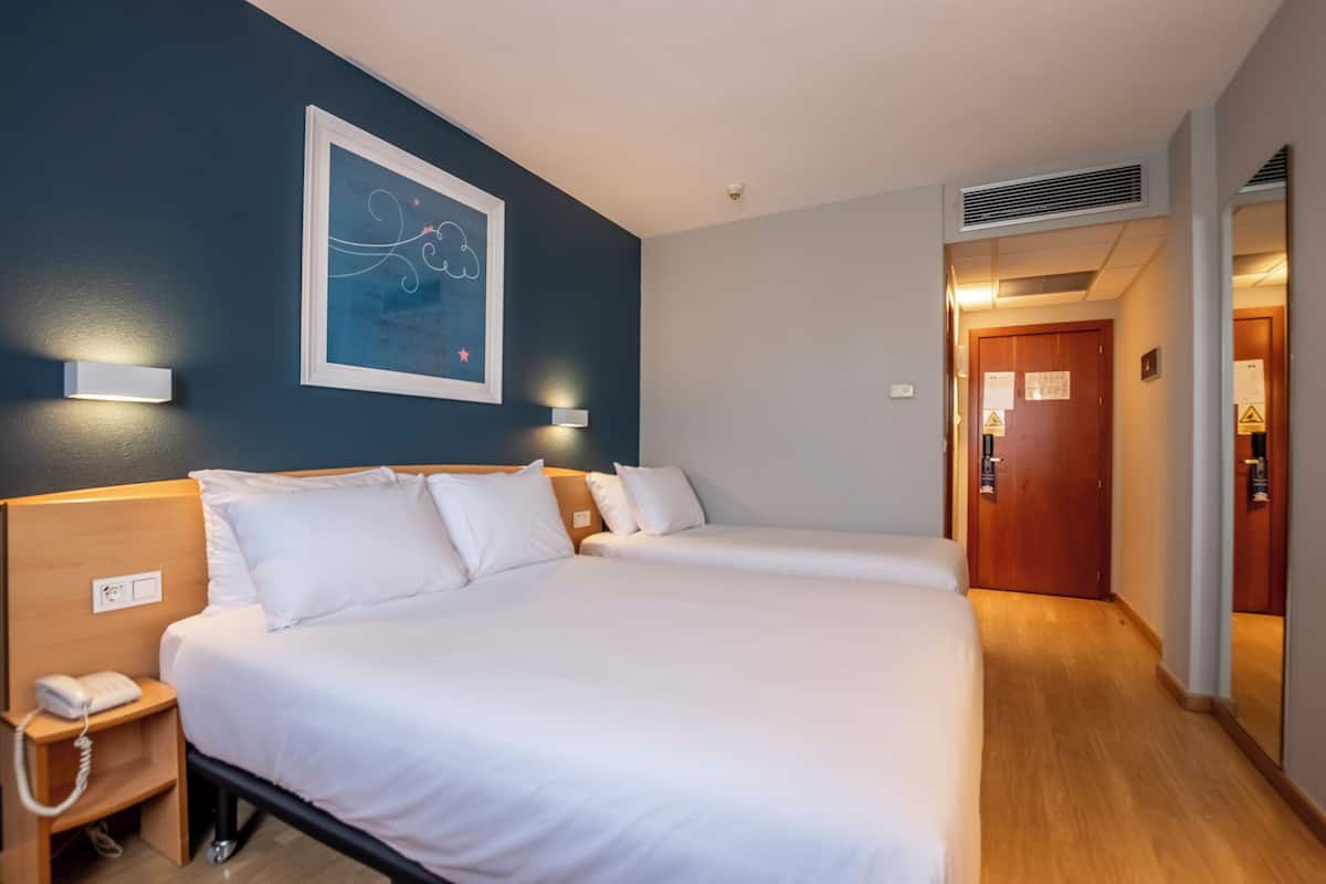 A hotel room with two beds, a bedside phone, wall-mounted lights, and a framed artwork on the wall.