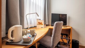 Habitación de hotel con escritorio de madera, una silla, televisor, tetera, bandeja con tazas y una taza, y un menú en la pared.