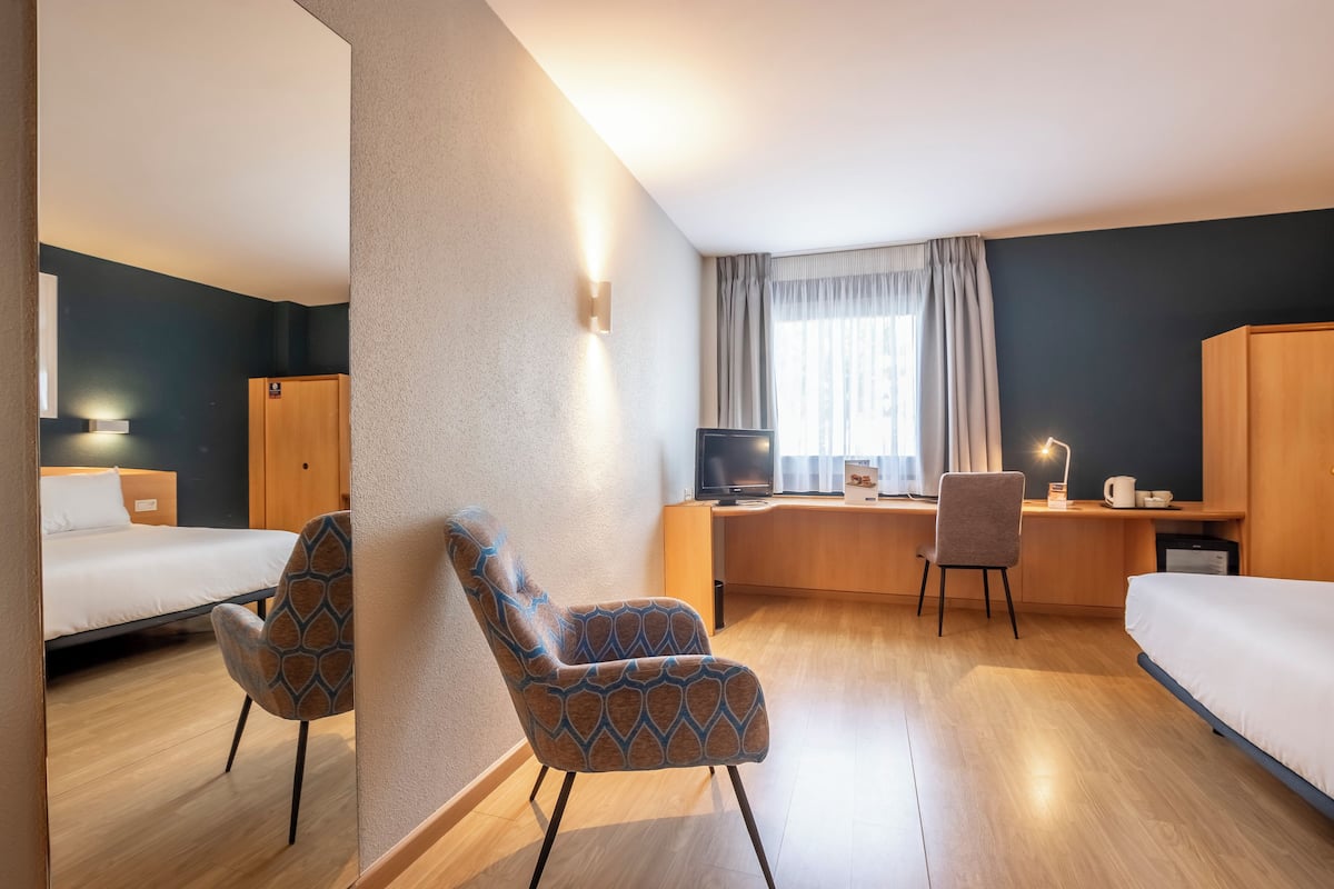 A hotel room with a bed, a desk, a chair, and a television.