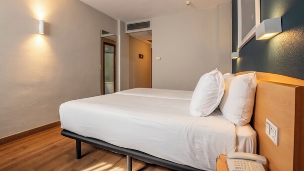 Una habitación de hotel con una cama, mesita de noche y teléfono en la pared.