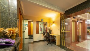 A reception area with a marble counter, a desk with chairs, a clock, and an elevator. - Real Castilha Hotel (São Paulo)