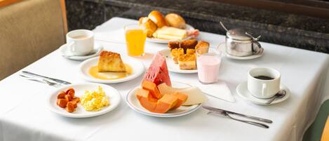 A breakfast table with plates of food, including toast, eggs, and fruit, and cups of coffee and juice.