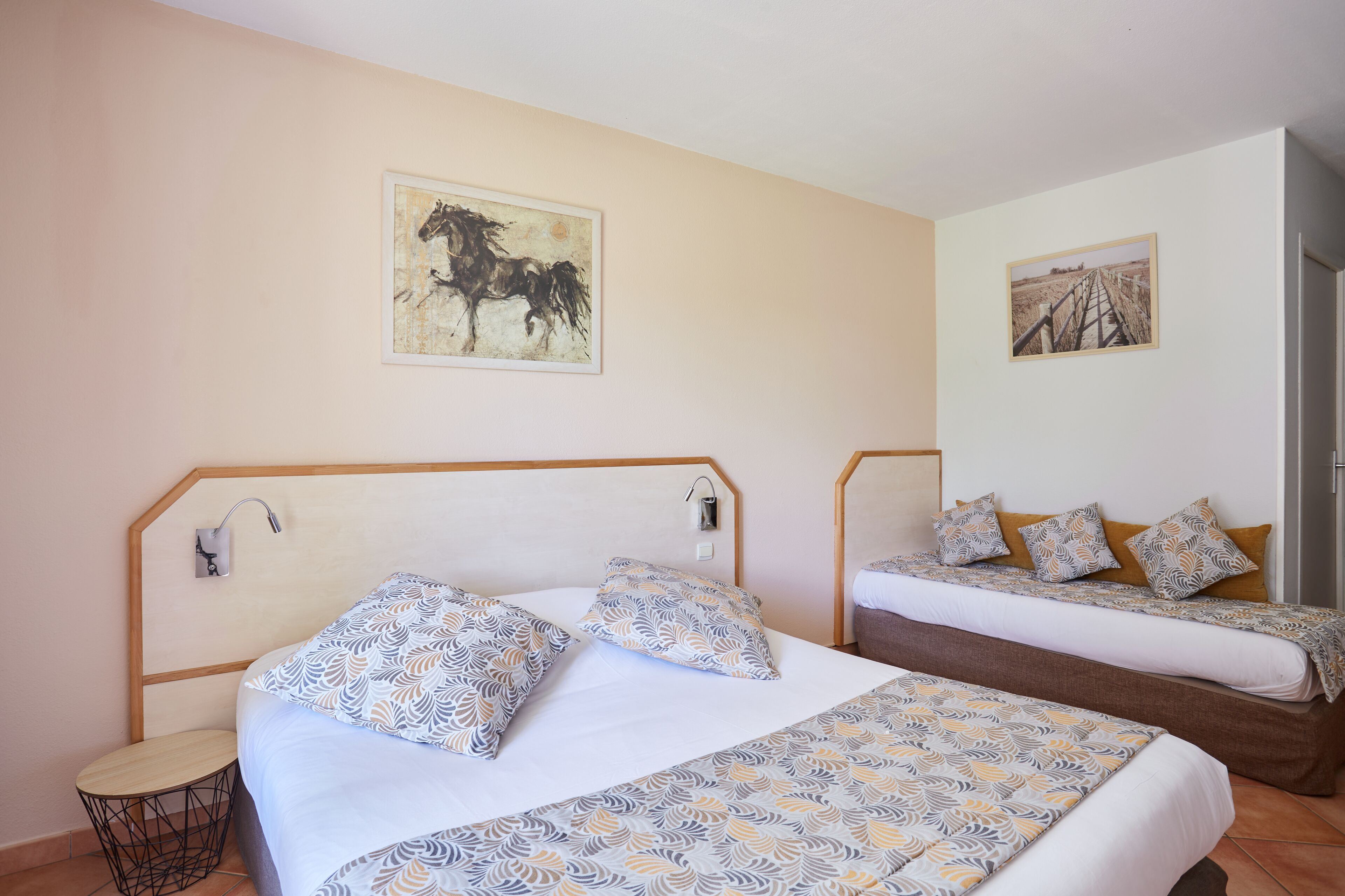 A bedroom with two beds, a small round table, and two wall-mounted lamps.