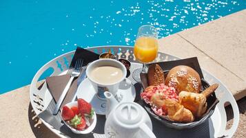 Ein Frühstücksbrett mit Kaffee, Saft, Erdbeeren, Croissants und einem Teekessel am Pool.