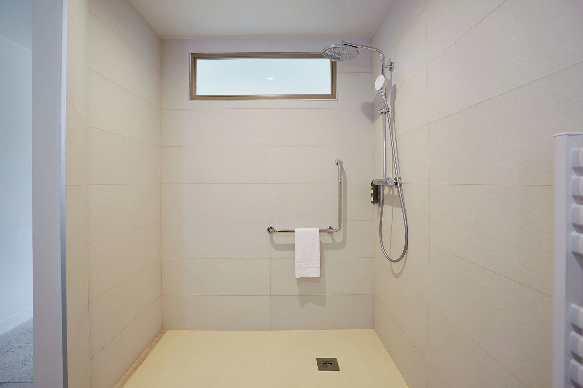 Pequeno espaço de duche fechado com um chuveiro manual, outro chuveiro manual e um porta-toalhas com uma toalha.