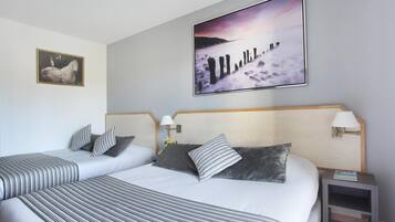 Habitación de hotel con dos camas, un cuadro grande de una escena costera, un retrato enmarcado de un caballo y una pequeña mesa con una lámpara.