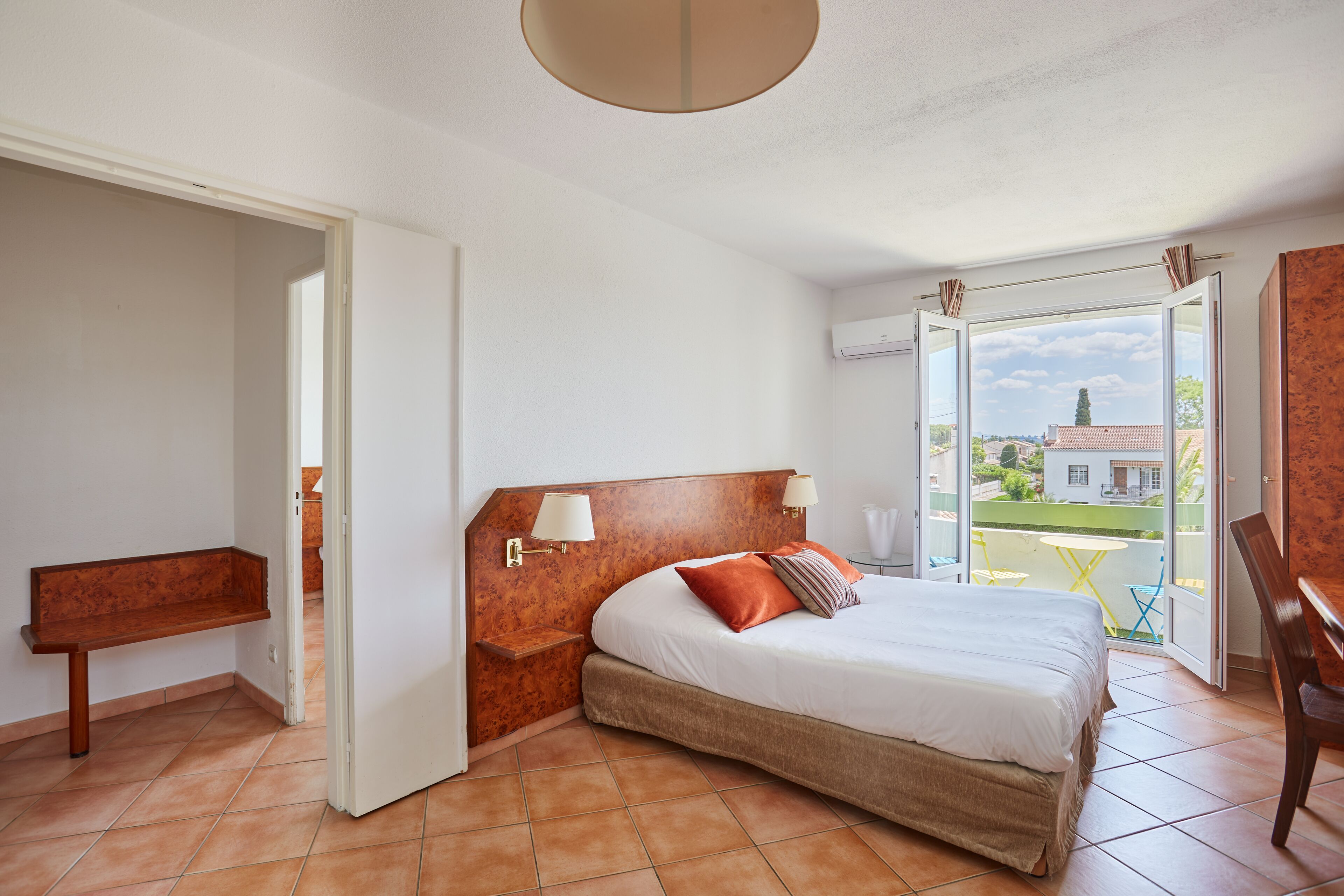 A bedroom with a bed, bedside tables, a bench, and a view of the outside.