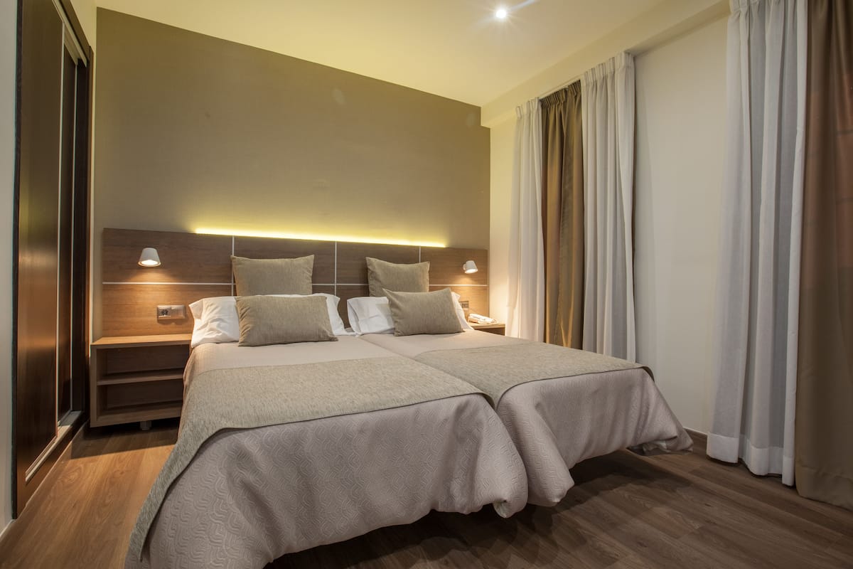 Cama doble con cabecera, mesitas de noche y lámpara fijada a la pared.