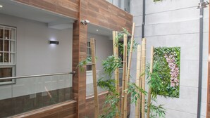 Un interior de varios niveles con paneles de madera, barandilla de cristal y jardines verticales.