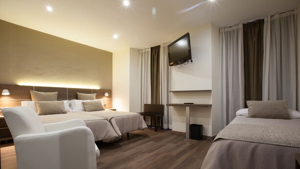 Habitación de hotel con dos camas, un televisor montado en la pared y un escritorio con silla.