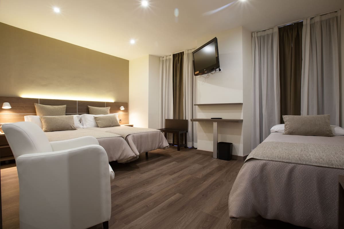 Una habitación de hotel con dos camas, un televisor montado en la pared, un escritorio y una silla.