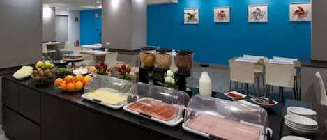 A buffet area with various food items and a blue wall with framed artwork.