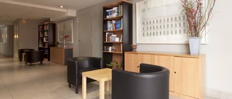 A modern waiting area with leather chairs, a wooden table, a bookshelf, and a potted plant.