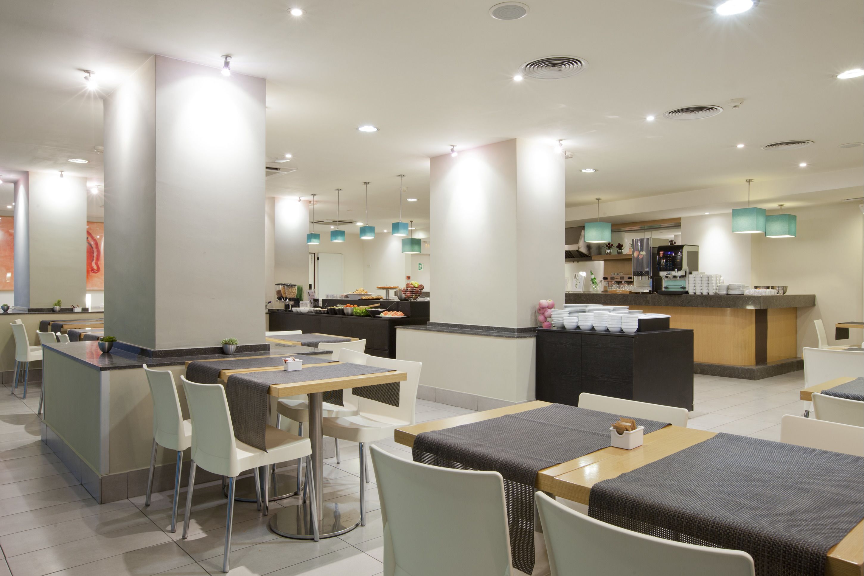 A modern restaurant with a central bar area, multiple dining tables, and a kitchen in the background.