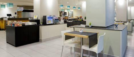 A modern hotel lobby with a reception desk, seating area, and a kitchenette.