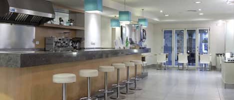 A modern bar area with a long counter, multiple stools, and overhead lighting.