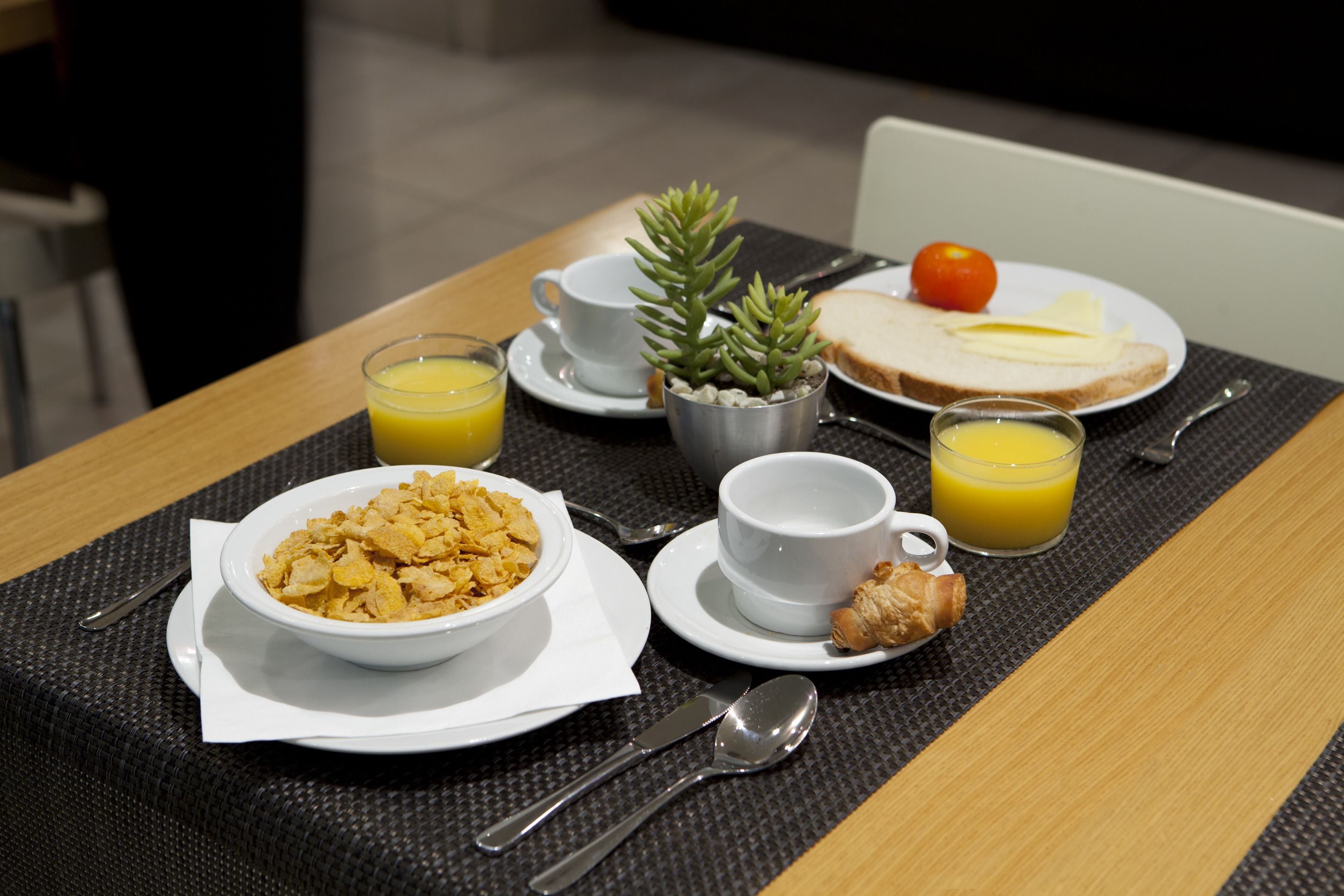 A breakfast setting with cereal, toast, juice, and a small plant on a table.