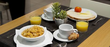 A breakfast setting with cereal, toast, juice, and a small plant on a table.