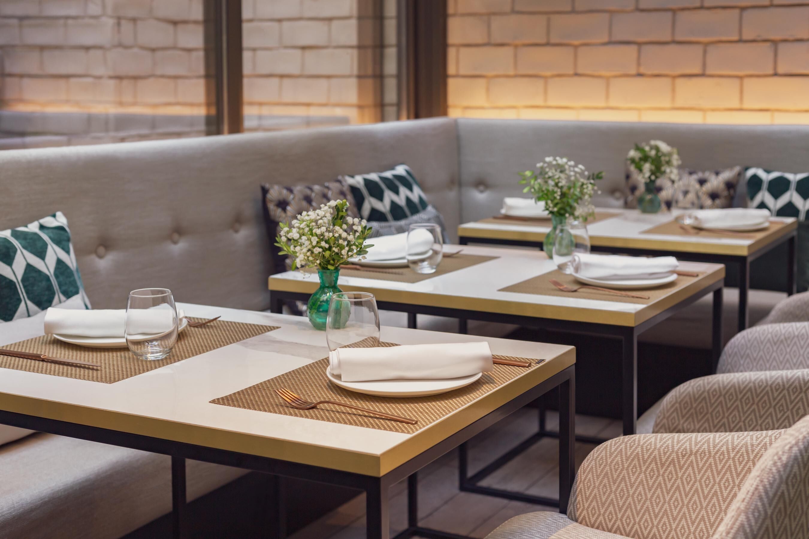 Un restaurante con una decoración moderna, que presenta asientos acolchados y mesas dispuestas con servilletas blancas, platos y copas.
