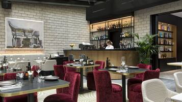 Un restaurante moderno con paredes de ladrillo, una zona de bar con estantes llenos de botellas y sillas tapizadas en rojo y blanco.