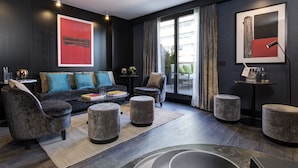 Uma sala de estar moderna com cores escuras, apresentando um sofá, poltronas, pufes e uma mesa de centro.