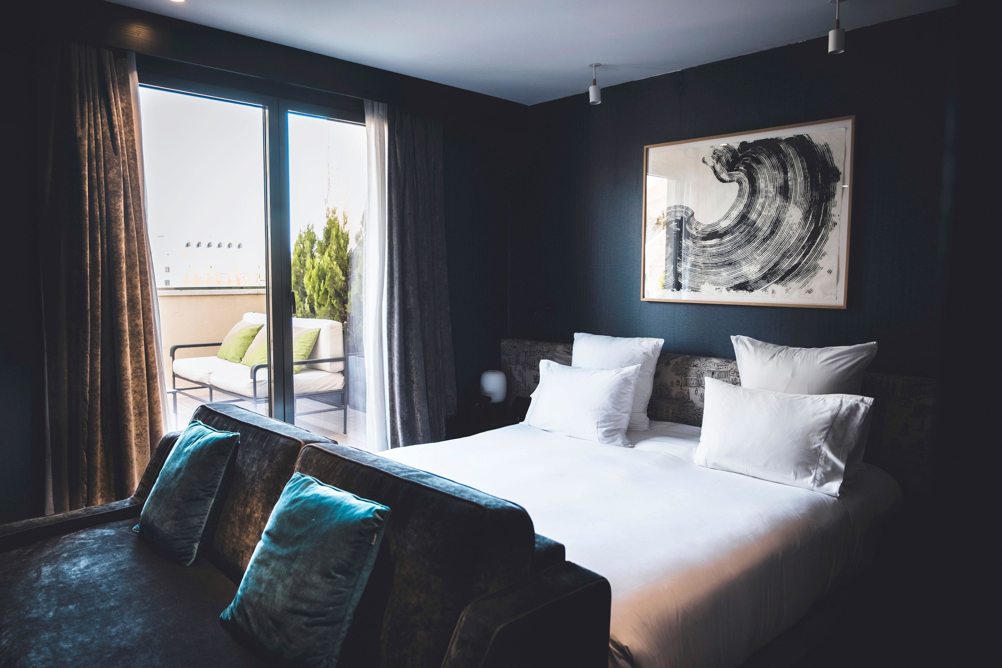 Habitación de hotel con una cama grande, vistas a un balcón y una obra de arte abstracta en la pared.
