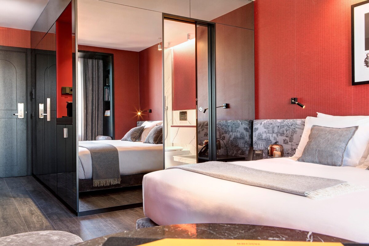 Une chambre d’hôtel avec un grand lit, un lit plus petit, une armoire et un miroir.