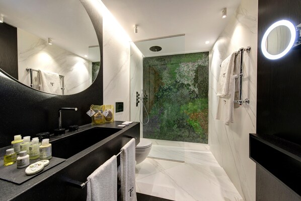 Un baño moderno con un lavamanos negro, paredes de mármol blanco, un espejo grande y una cabina de ducha de vidrio.