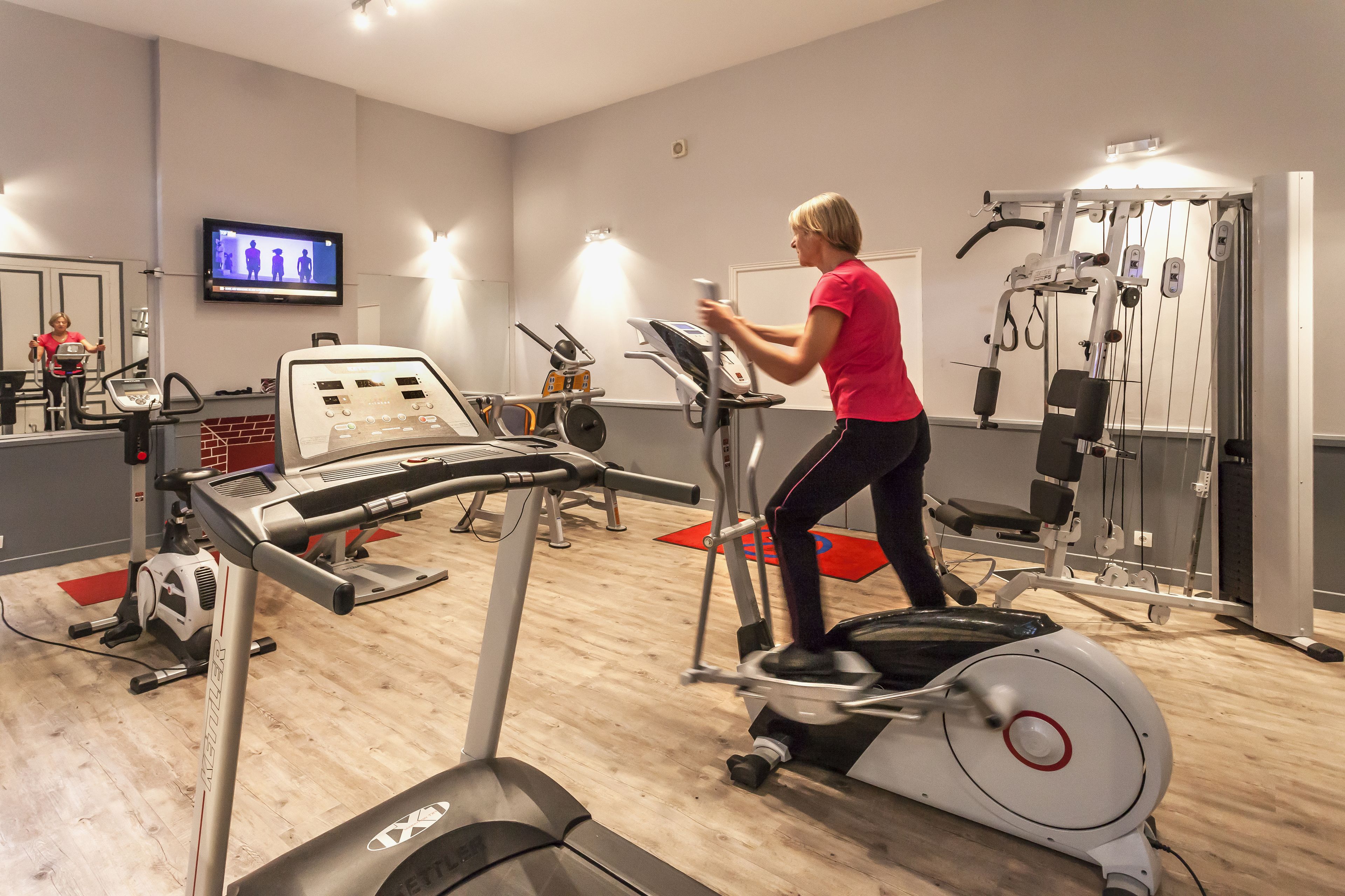 Une salle de sport équipée d’appareils de cardio, d’un téléviseur et d’un miroir.